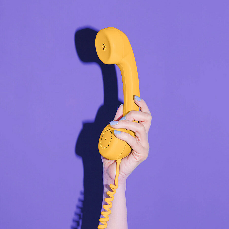 Hand hält gelben Telefonhörer vor lila Hintergrund