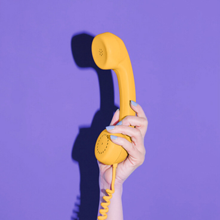 Hand holding yellow phone in front of purple background